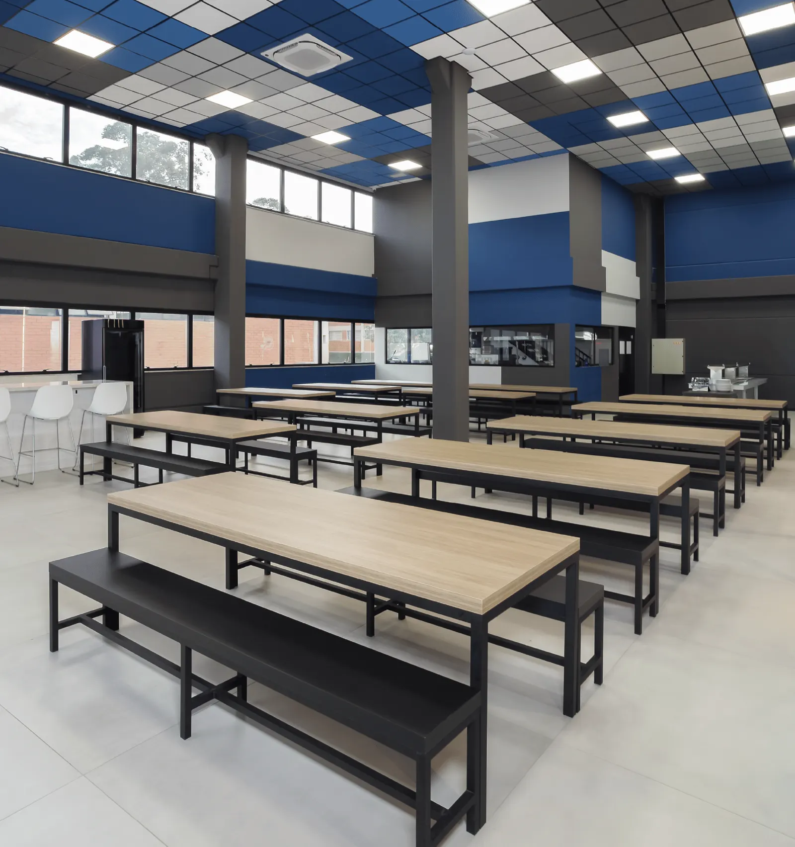 Espaço de coffee break com mesas coletivas de madeira e teto azul e branco